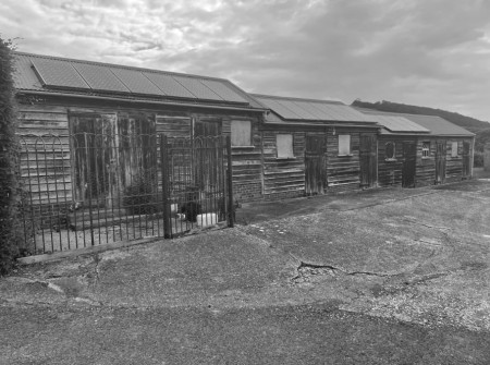 Black and white image of 2 wooden stable buildings and stable yard. Solar panel on the roofs.