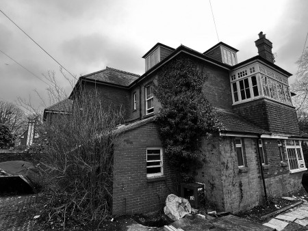 Black and white photo of a semi derelict residential building. Ivy growing up one side of the building.